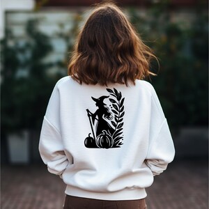 May include: White sweatshirt with a black silhouette of a witch holding a broom and standing in front of pumpkins and leaves.