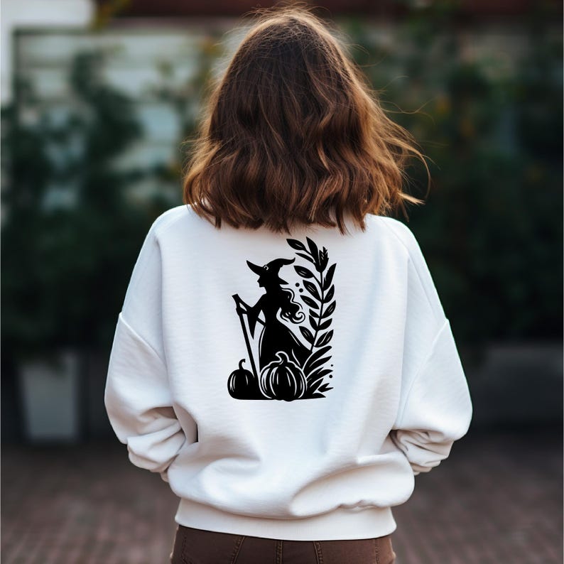 May include: White sweatshirt with a black silhouette of a witch holding a broom and standing in front of pumpkins and leaves.