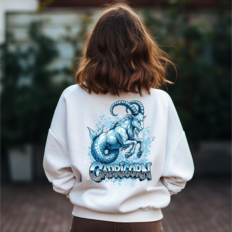 May include: White sweatshirt featuring a blue and white Capricorn graphic on the back. The design depicts a mythical creature with a goat head and fish tail, with the word "CAPRICORN" in a stylized font.