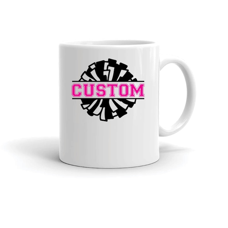 May include: White ceramic coffee mug with a black and white cheerleading pom pom graphic and the word "CUSTOM" in pink lettering.