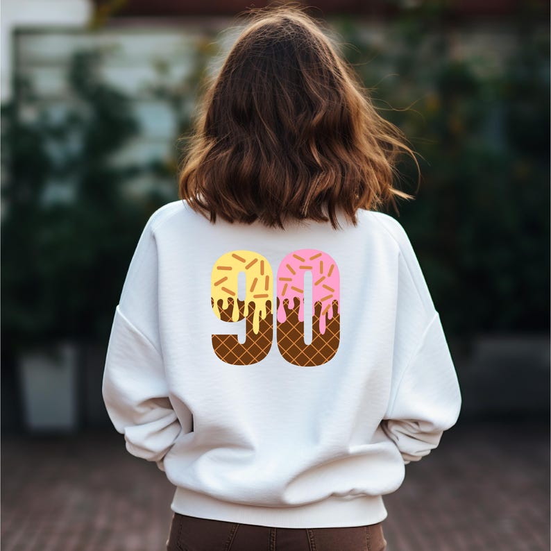 May include: White sweatshirt with a graphic of the number 90 made to look like an ice cream cone with yellow and pink ice cream and chocolate sprinkles.