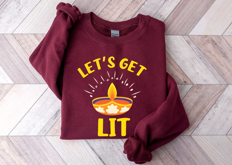 May include: A maroon sweatshirt with the text 'LET'S GET LIT' in yellow. The text is above a yellow diya with a flame and orange and white details.