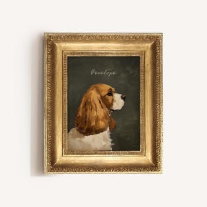 May include: A framed portrait of a Cavalier King Charles Spaniel dog, with brown and white fur, set against a dark green background. The dog is facing right, with the name "Penelope" written above. The frame is gold.