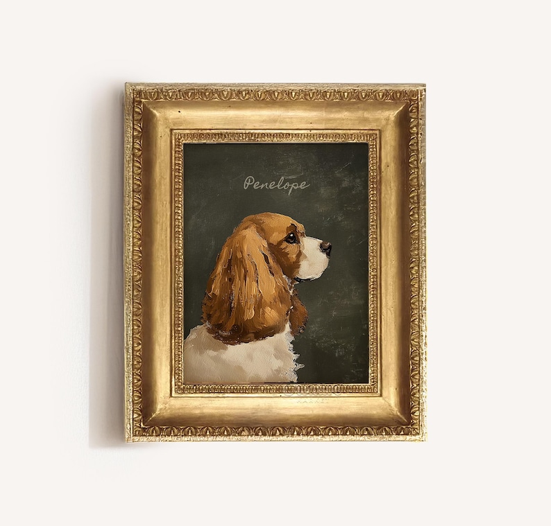 May include: A framed portrait of a Cavalier King Charles Spaniel dog, with brown and white fur, set against a dark green background. The dog is facing right, with the name "Penelope" written above. The frame is gold.
