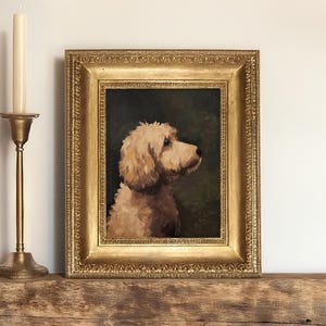 Op de afbeelding: Een ingelijst olieverfschilderij van een lichtbruine hond met zijn hoofd naar rechts gedraaid. De hond kijkt naar de zijkant. Het schilderij is in een gouden lijst met sierlijke details.