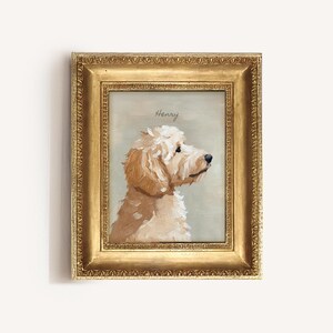 May include: A framed portrait of a dog, painted in shades of cream and tan, with the name "Henry" above the dog's head. The dog is facing right, with a fluffy coat and dark eyes. The frame is gold.