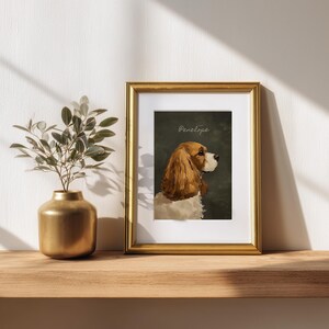 May include: A framed portrait of a Cavalier King Charles Spaniel named Penelope. The dog is depicted in profile with brown and white fur against a dark green background. The gold frame sits on a wooden shelf next to a gold vase with greenery.