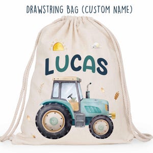 Puede incluir: Una bolsa con cordón beige con un diseño de tractor y el nombre "LUCAS" en verde azulado y azul marino. La bolsa presenta un tractor azul con neumáticos negros, un sol amarillo y el texto "DRAWSTRING BAG (CUSTOM NAME)".