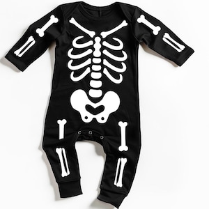 Könnte beinhalten: Schwarzer Baby-Overall mit weißem Skelett-Design. Der langärmlige Anzug zeigt einen detaillierten Brustkorb, eine Wirbelsäule und Knochen, ideal für Halloween. Der Overall hat Druckknöpfe für einfaches An- und Ausziehen.