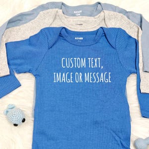 Könnte beinhalten: Ein blauer langärmliger Baby-Body mit dem Text "CUSTOM TEXT, IMAGE OR MESSAGE" auf der Vorderseite. Der Body ist aus weichem, geripptem Stoff.