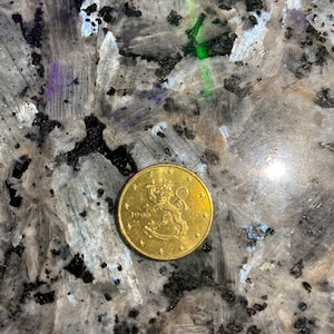 Puede incluir: Una moneda de color dorado con un león y el año 1999 en ella. La moneda tiene un círculo de estrellas alrededor del borde.