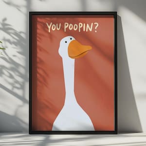 Könnte beinhalten: Ein gerahmter Kunstdruck, der eine weiße Gans mit orangefarbenem Schnabel vor einem einfarbigen terrakottafarbenen Hintergrund zeigt. Der Text "YOU POOPIN?" steht in einer einfachen, hellen Schrift über dem Kopf der Gans im schwarzen Rahmen.
