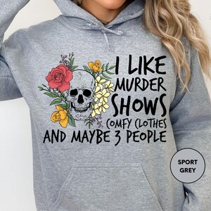 a woman wearing a grey hoodie with a skull and flowers on it