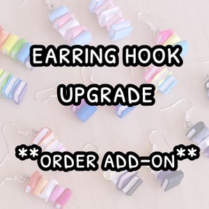 May include: A close-up of several pairs of colorful book stack earrings with silver earring hooks. The text "EARRING HOOK UPGRADE **ORDER ADD-ON**" is displayed on the image.