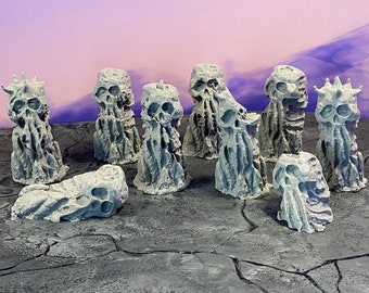 May include: A collection of eight gray, skeletal, and textured miniature figurines with a ninth figurine lying on its side. The figurines are arranged on a gray, cracked surface.