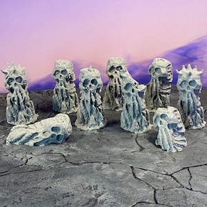 Puede incluir: Una colección de ocho figuritas en miniatura grises, esqueléticas y texturizadas, con una novena figurita tumbada de lado. Las figuritas están dispuestas sobre una superficie gris y agrietada.