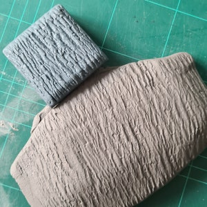 May include: Two pieces of grey textured material, one is a square and the other is a larger rectangle. The texture resembles tree bark.