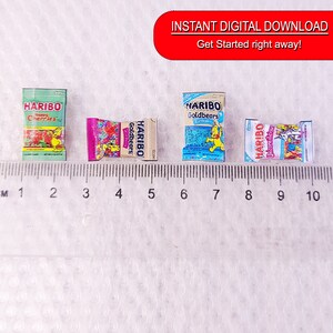 May include: Four miniature boxes of Haribo gummy candies. The boxes are arranged in a row on a white surface with a ruler underneath. The boxes are labeled "Haribo Cherries", "Haribo Goldbears", "Haribo Goldbears", and "Haribo Unicemilicious".