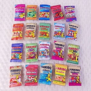 May include: A collection of 18 small bags of Haribo gummy candies. The bags are arranged in three rows of six. Each bag features a different flavor and design, including Happy Cola, Dinosaurs, Goldbears, Twin Snakes, Unicornlicious, Sour Bites, Watermelon, Peaches, and Star Mix.