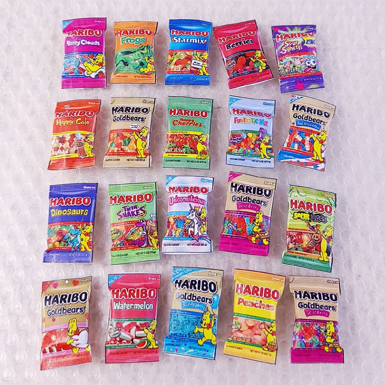 May include: A collection of 18 small bags of Haribo gummy candies. The bags are arranged in three rows of six. Each bag features a different flavor and design, including Happy Cola, Dinosaurs, Goldbears, Twin Snakes, Unicornlicious, Sour Bites, Watermelon, Peaches, and Star Mix.