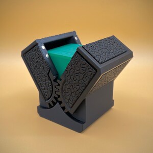 May include: A black card holder with a gear mechanism and a textured surface. The holder is open and a stack of green cards is visible inside.
