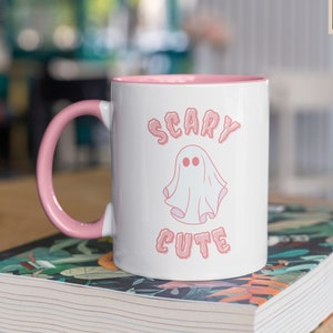 May include: White ceramic mug with a pink rim and handle. The mug features a pink ghost with the text "Scary Cute" in pink letters.
