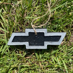 May include: A black and silver car ornament shaped like a bowtie with a string for hanging.