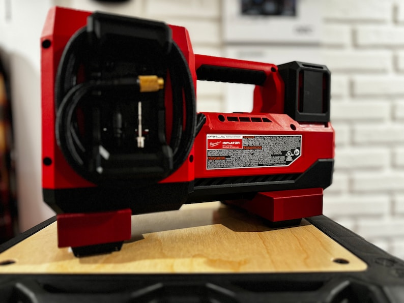 May include: A red and black cordless air compressor with a black hose and a black handle. The compressor is labeled "INFLATOR" and has a black and red battery pack.