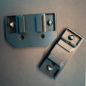 May include: Three black plastic camera mounting plates with screw holes. The plates are designed to attach to a camera or other equipment.
