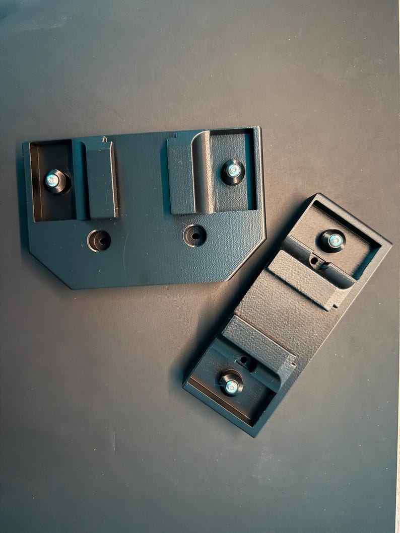 May include: Three black plastic camera mounting plates with screw holes. The plates are designed to attach to a camera or other equipment.