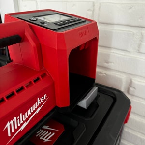 May include: A red Milwaukee M18 power tool with a black display screen and a silver metal attachment. The tool is sitting on top of a black toolbox.