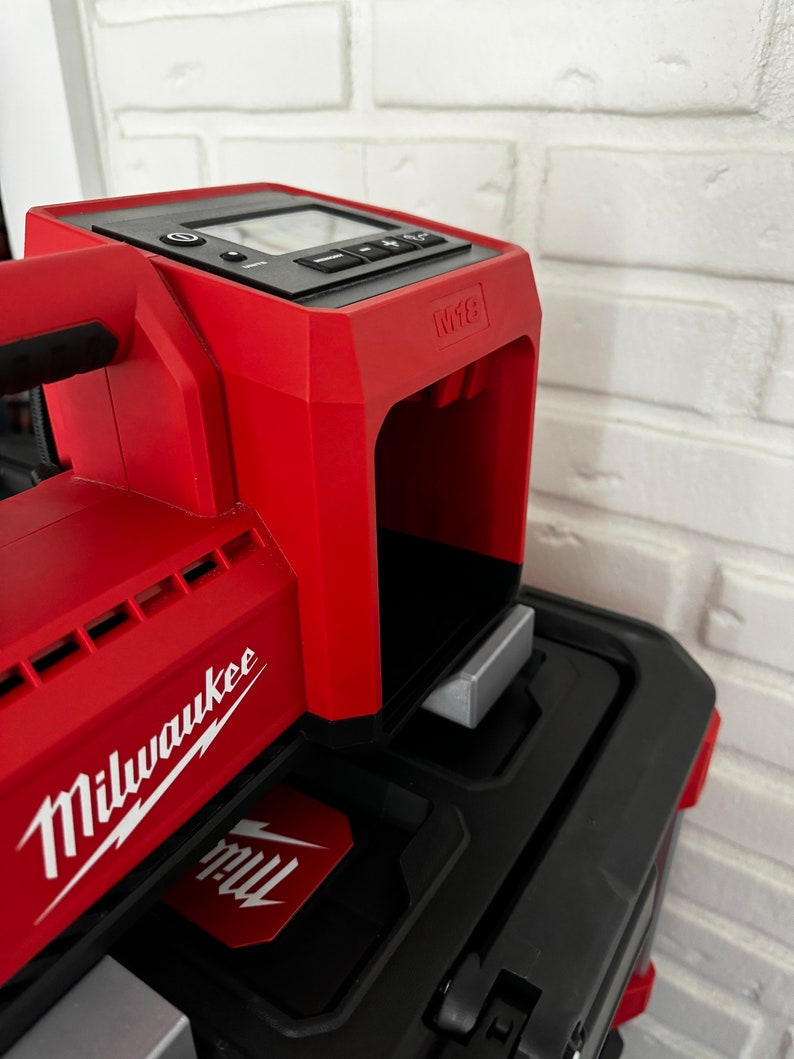 May include: A red Milwaukee M18 power tool with a black display screen and a silver metal attachment. The tool is sitting on top of a black toolbox.