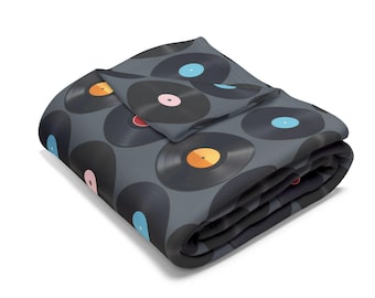 May include: A gray fleece blanket with a pattern of colorful vinyl records. The blanket is folded in half and the edges are visible.