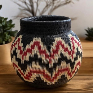 Peut inclure: Un panier rond en osier noir, blanc et rouge avec un motif géométrique. Le panier a une large ouverture.