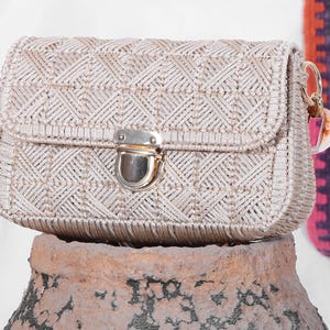 May include: A beige woven handbag with a gold clasp closure. The bag has a geometric pattern and a short strap.