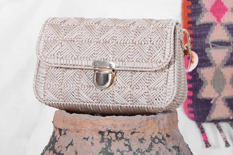 May include: A beige woven handbag with a gold clasp closure. The bag has a geometric pattern and a short strap.