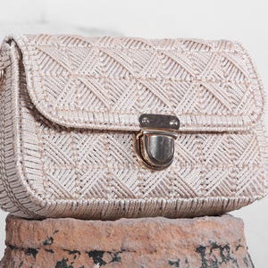 May include: A white woven crossbody bag with a gold clasp closure. The bag has a geometric pattern and is made of a thick, textured material.