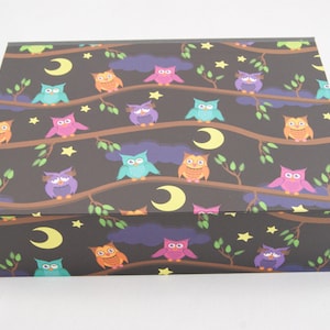 May include: A rectangular box with a dark background featuring a repeating pattern of colourful owls perched on tree branches. The owls are in various colours, with yellow moons and stars scattered throughout the design.