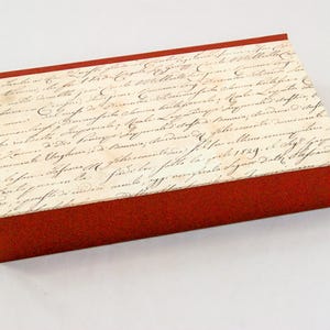 Peut inclure: Une boîte rectangulaire rouge avec un couvercle recouvert d'une écriture délavée. La boîte a une esthétique vintage, la surface blanc cassé du couvercle contrastant avec les côtés rouges.