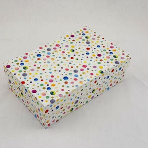 Op de afbeelding: Rechthoekige geschenkdoos met een witte basis, versierd met veelkleurige stippen. De stippen variëren in grootte en kleur, waaronder blauw, geel, roze en groen. De doos is gesloten.