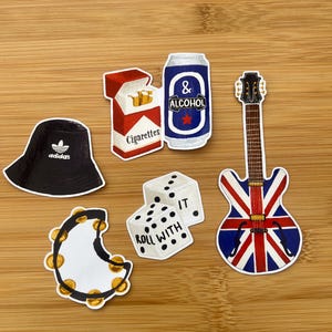 Może przedstawiać: Zestaw naklejek przedstawiających czarny kapelusz Adidas, paczkę papierosów, puszkę alkoholu, gitarę z motywem Union Jack, kostki do gry z napisem "Roll with it" i tamburyn.
