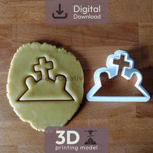 Może przedstawiać: Wycinak do ciastek w kształcie nagrobka i wycięte ciastko na drewnianej powierzchni. Wycinak do ciastek jest z białego plastiku, a ciastko ma jasnobrązowy kolor. Wycinak do ciastek i ciastko mają na górze krzyż. Obraz zawiera tekst "Pobieranie cyfrowe" i "Model druku 3D".