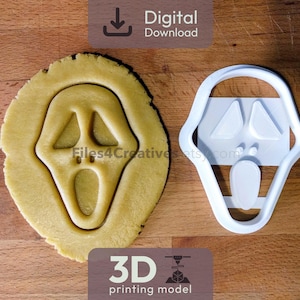May include: A cookie cutter and a cookie in the shape of a Scream mask are displayed on a wooden surface. The cookie cutter is white, and the cookie is light brown. The image includes the text "Digital Download" and "3D printing model".