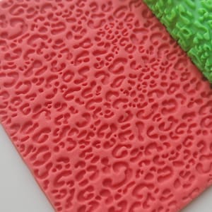 May include: A close-up of a pink textured sheet and a green rolling pin. The sheet has a leopard print pattern. The rolling pin is green and has a matching leopard print pattern. The items are likely for baking or crafting.