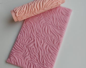 Puede incluir: Un rodillo rosa texturizado y una lámina rectangular rosa con un patrón ondulado similar. El rodillo es cilíndrico con un mango en cada extremo. La lámina es plana y rectangular, con una superficie texturizada en relieve.