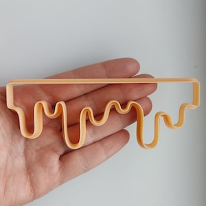 May include: A light orange plastic cookie cutter shaped like a dripping line of icing.