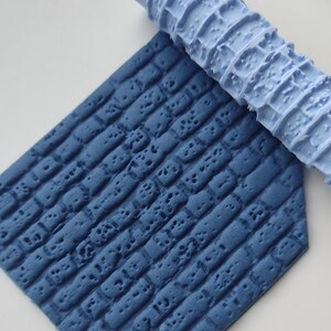 Könnte beinhalten: Eine blaue, strukturierte Teigrolle und eine passende blaue Oberfläche mit einem Ziegelmuster. Die Teigrolle ist zylindrisch mit einer strukturierten Oberfläche. Die Oberfläche ist sechseckig und flach mit einem Ziegelmuster.