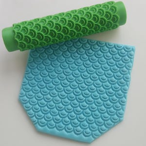 May include: A green rolling pin with a scale pattern and a blue silicone mat with a scale pattern.