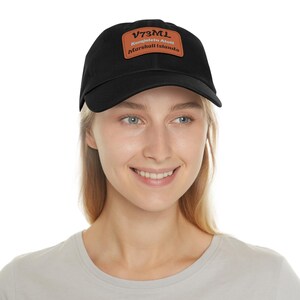 Puede incluir: Una gorra de béisbol negra con un parche de cuero marrón que dice "V73ML Kwajalein Atoll Marshall Islands".