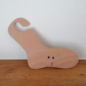 Peut inclure: Une forme de chaussure en bois de couleur claire avec une poignée incurvée. La forme a la forme d'un pied avec une section d'orteil articulée et deux œillets métalliques. La forme de chaussure repose sur une surface en bois.